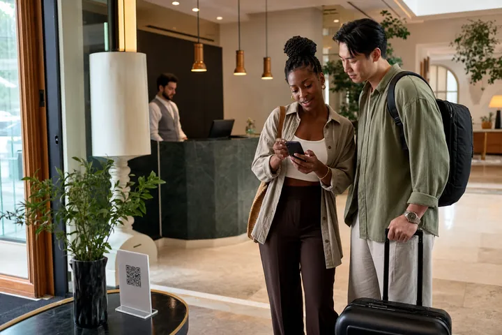 Călători internaționali care folosesc un catalog multilingv QR într-un hotel de tip boutique european